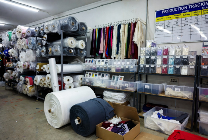 Organized fabric rolls, trims, and digital material status tracking in apparel warehouse, highlighting effective sourcing to reduce lead time in fashion production