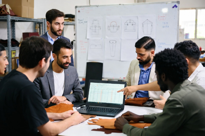 Collaborative sourcing meeting with leather samples, spreadsheets, and notes for practical small leather goods cost breakdown and negotiation