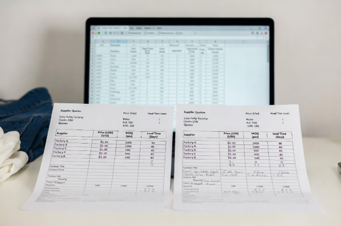 Side-by-side clothing factory quotes and spreadsheet analysis for price, MOQ, and terms comparison during sourcing negotiations with garment manufacturers
